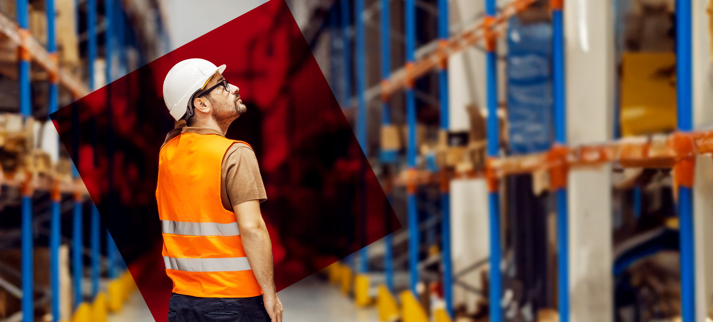 Senhor com um colete refletor e um capacete dentro de um armazém.