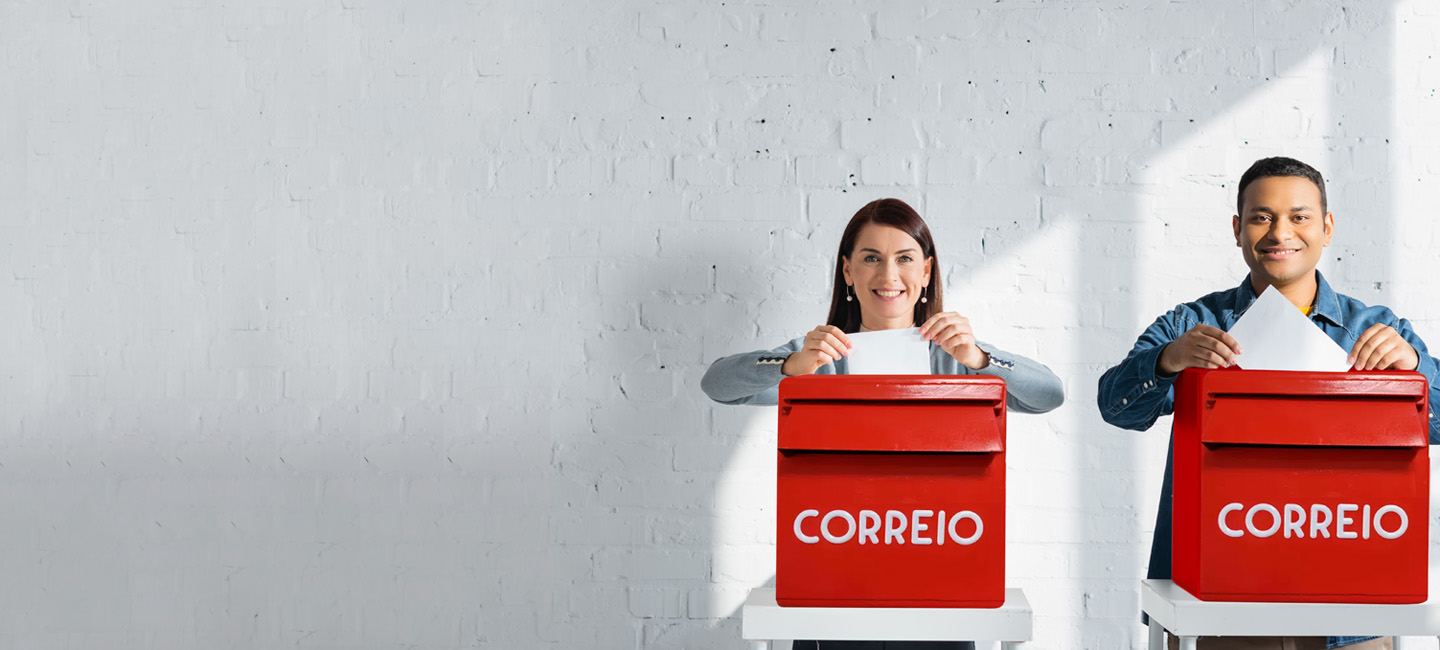 dois indivíduos a colocar um boletim de voto no marco de correio