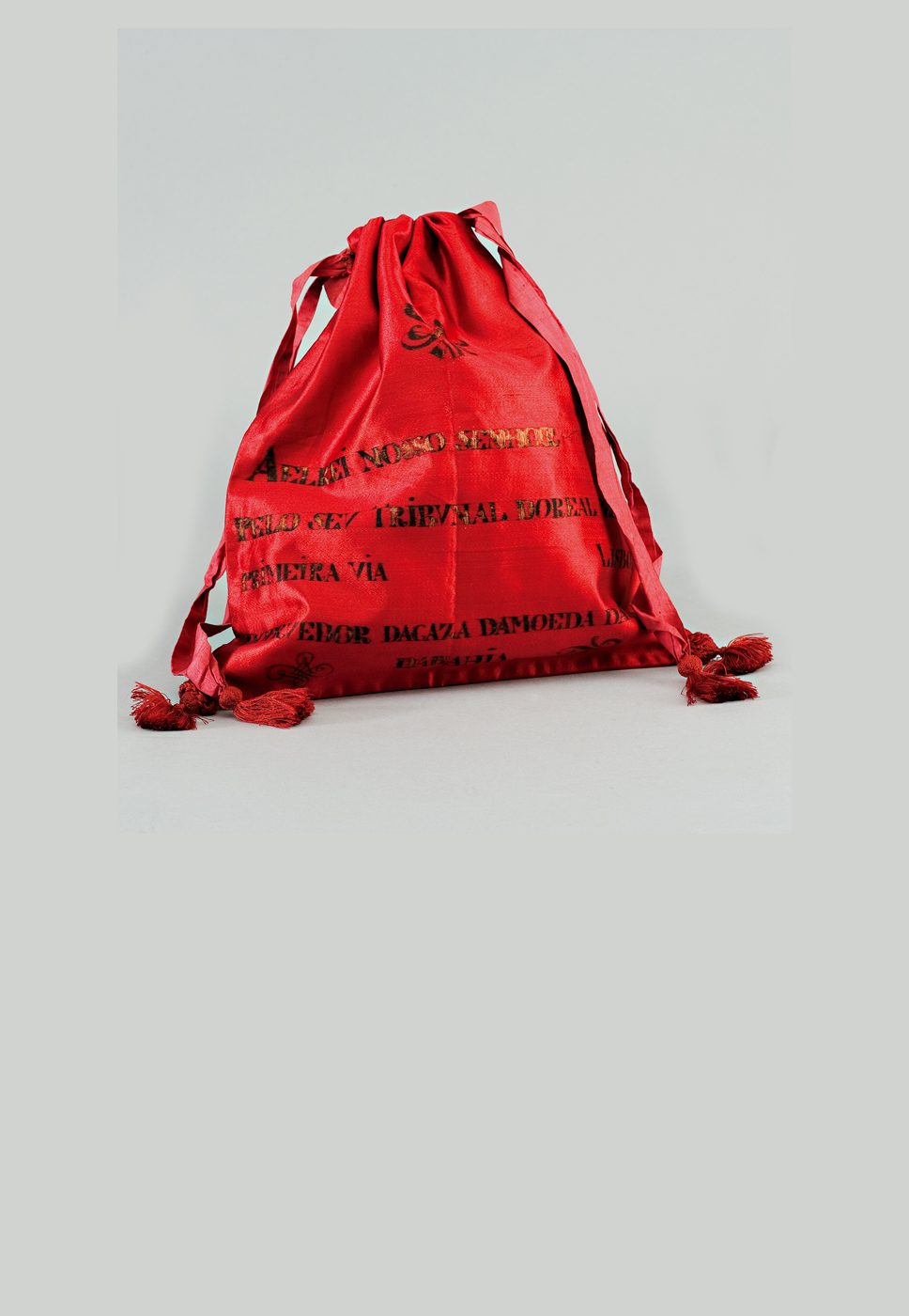 Duas mochilas de cordão, uma vermelha e outra branca com texto preto, sobre fundo cinza.