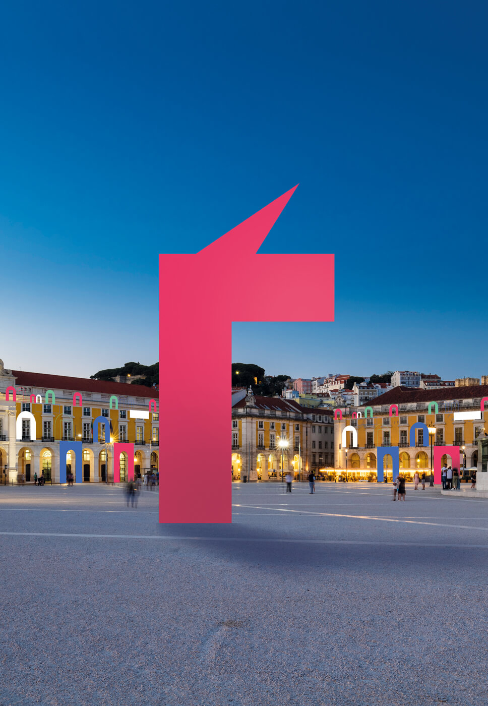 Praça iluminada ao entardecer com arco central, luzes coloridas e escultura vermelha moderna.