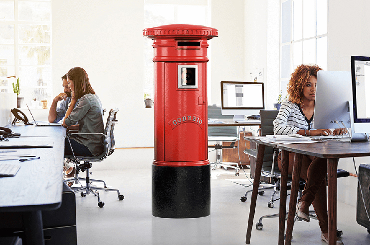 escritório com várias pessoas sentadas nas secretárias e um marco do Correio CTT ao centro